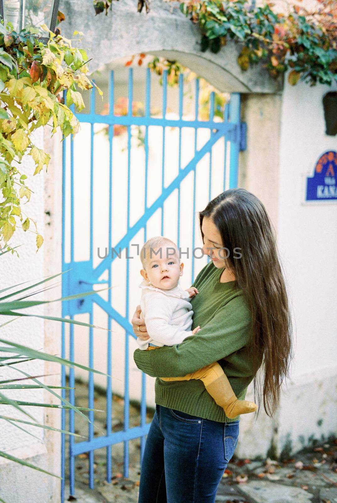 Mom with a baby in her arms stands in front of a metal gate. High quality photo