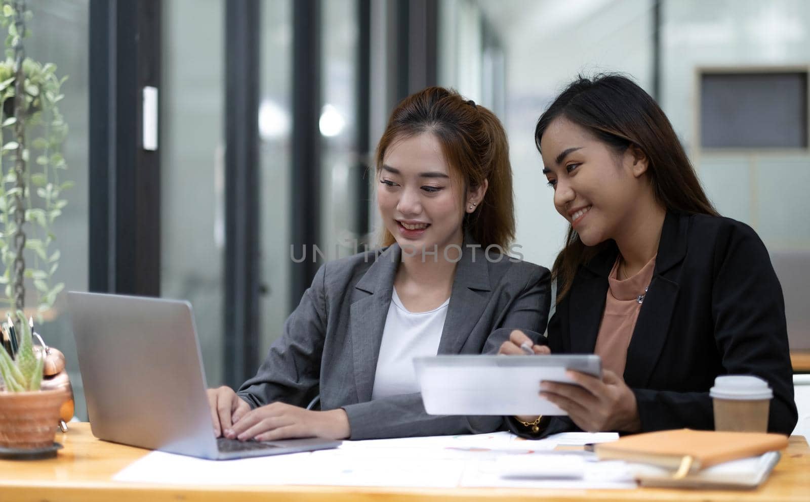 Two young Asian business woman talk, consult, discuss working with new startup project idea presentation analyze plan marketing and investment in the office. by wichayada