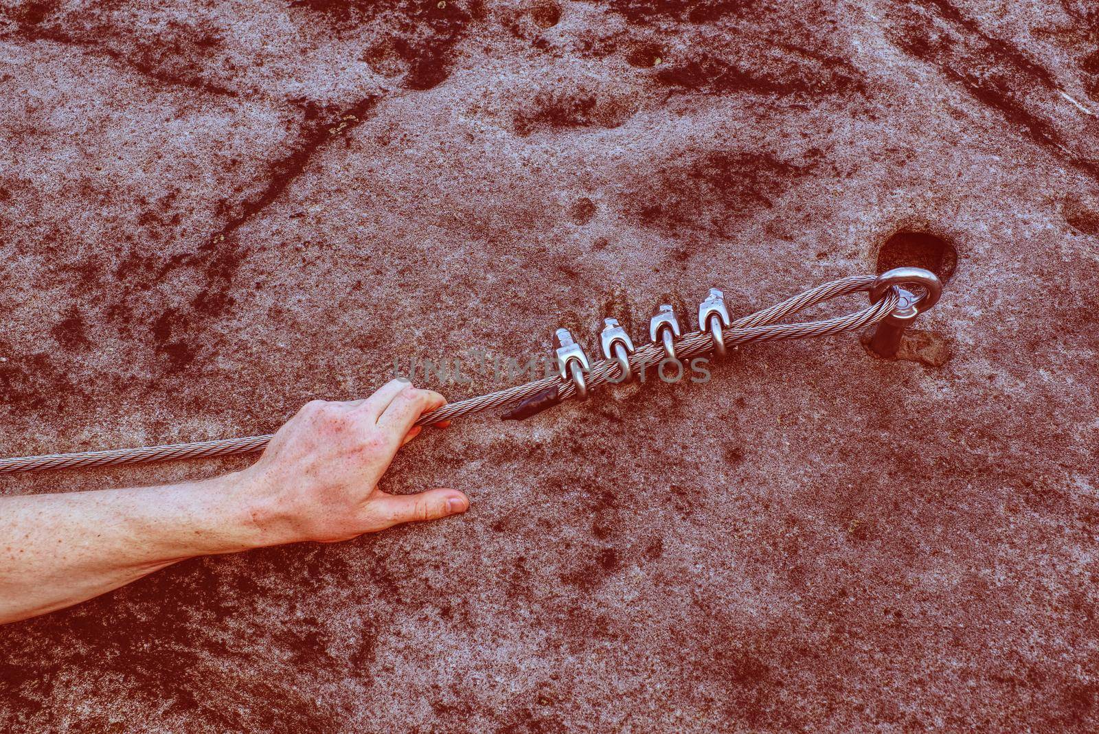 Climber's hand gripping metal rope at natural cliff  by rdonar2