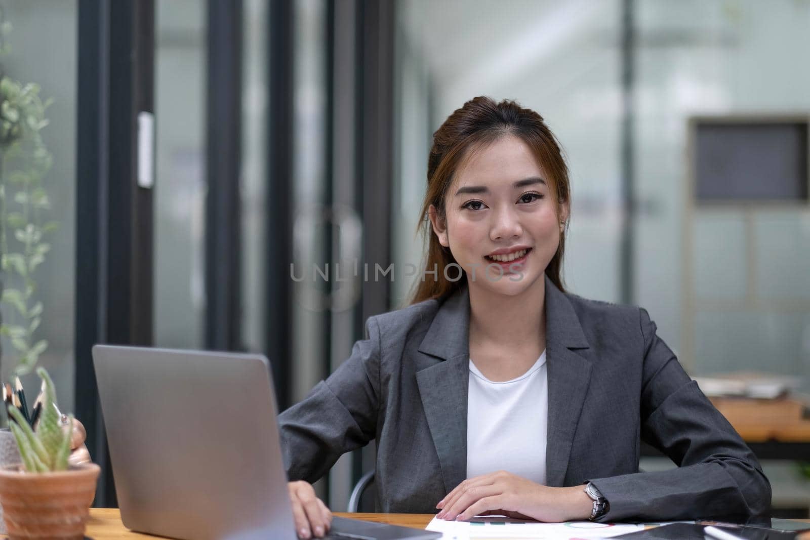 Happy young Asian businesswoman working on laptop keyboard with document at office . Looking at camera. by wichayada