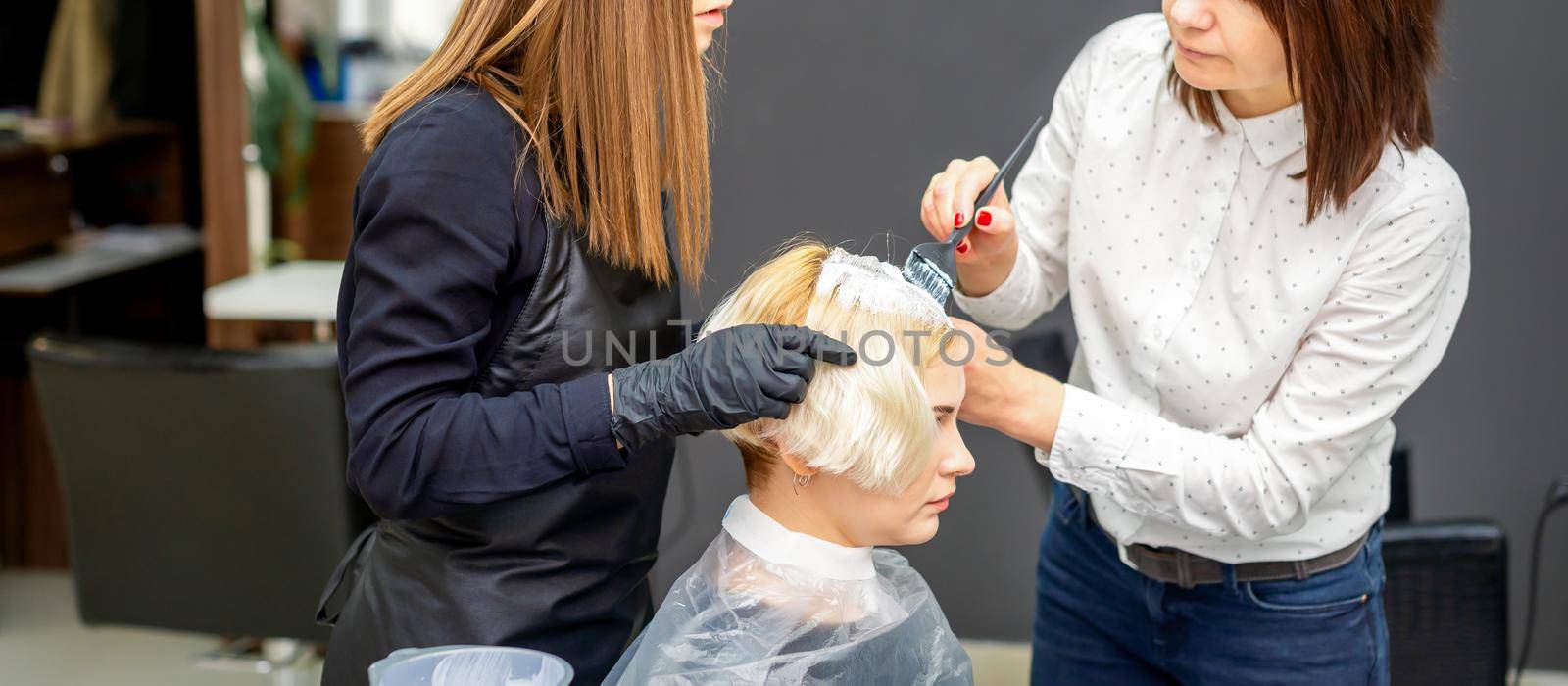 Two hairdressers dyeing hair of woman by okskukuruza