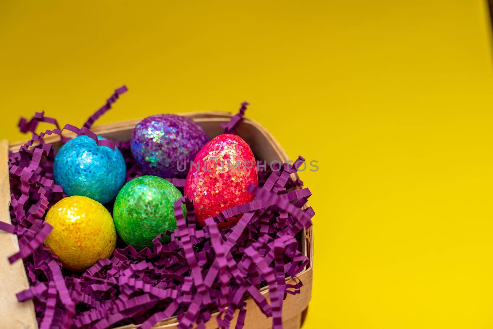 Easter composition from a basket and colored eggs prepared for the holiday on a yellow background.