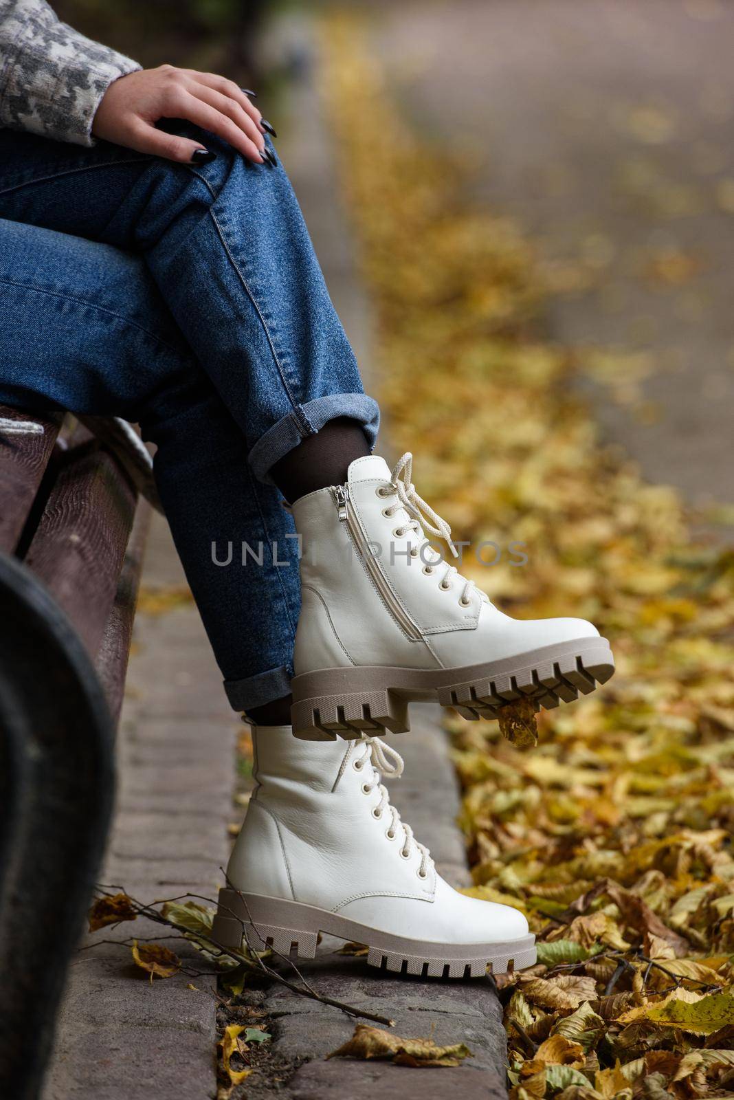 Female legs in a jeans and white fashion boots with laces. fallen leaves on the sidewalk