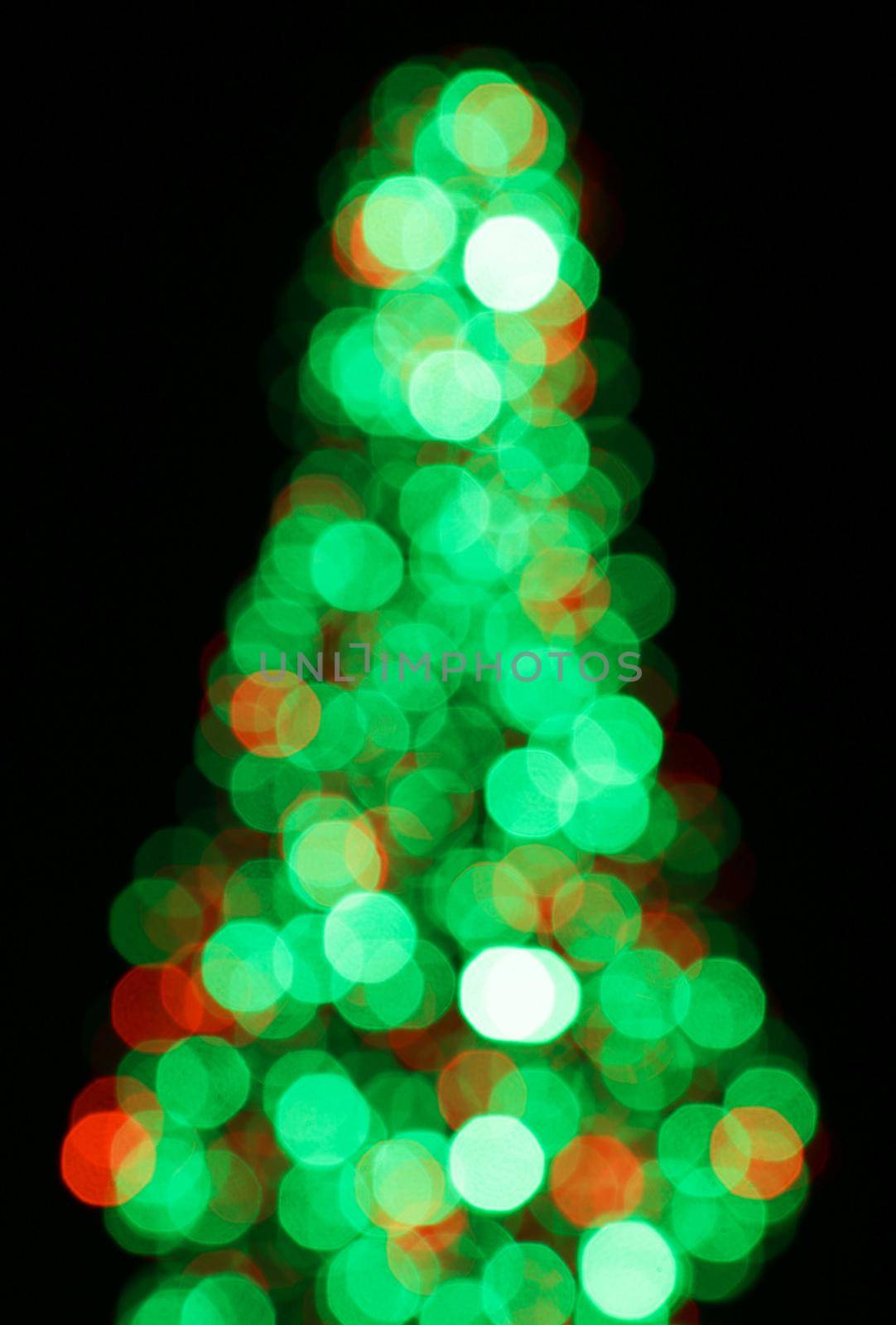 Blurred background, bokeh with colorful lights, holiday lighting. Abstract blur. Beautiful small Christmas tree.