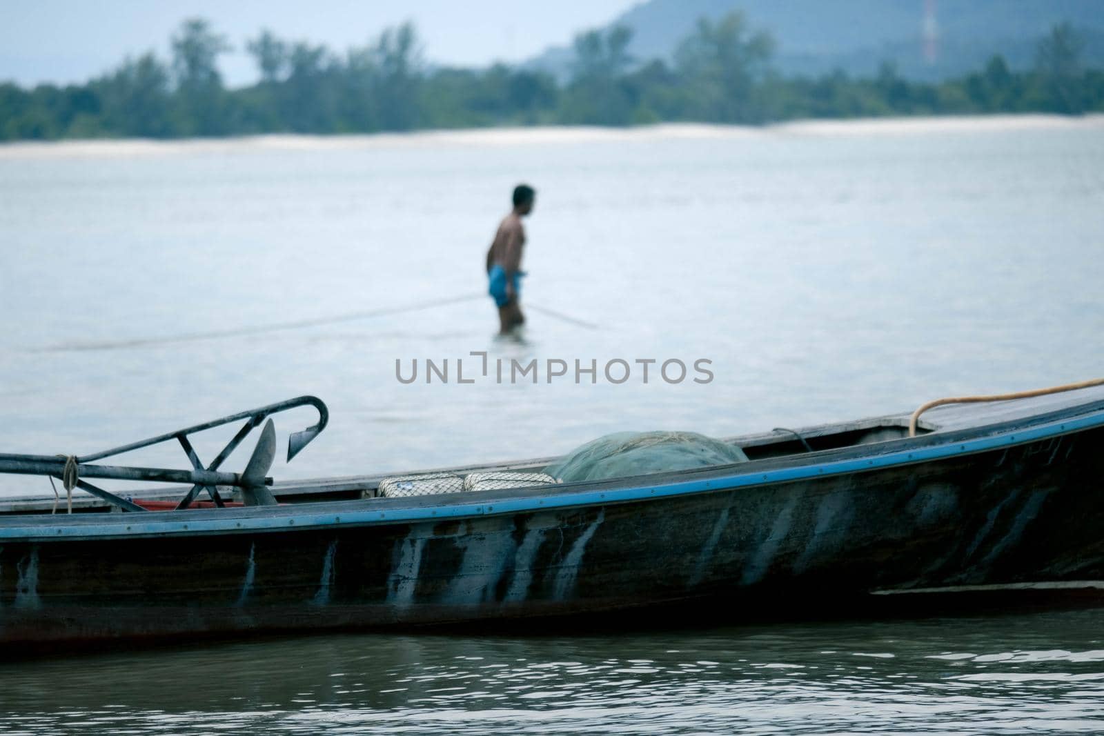 Thai small fishing boat moored on the beach with fishermen preparing to go fishing in the morning in the background. Life in the traditional Thai countryside. by TEERASAK