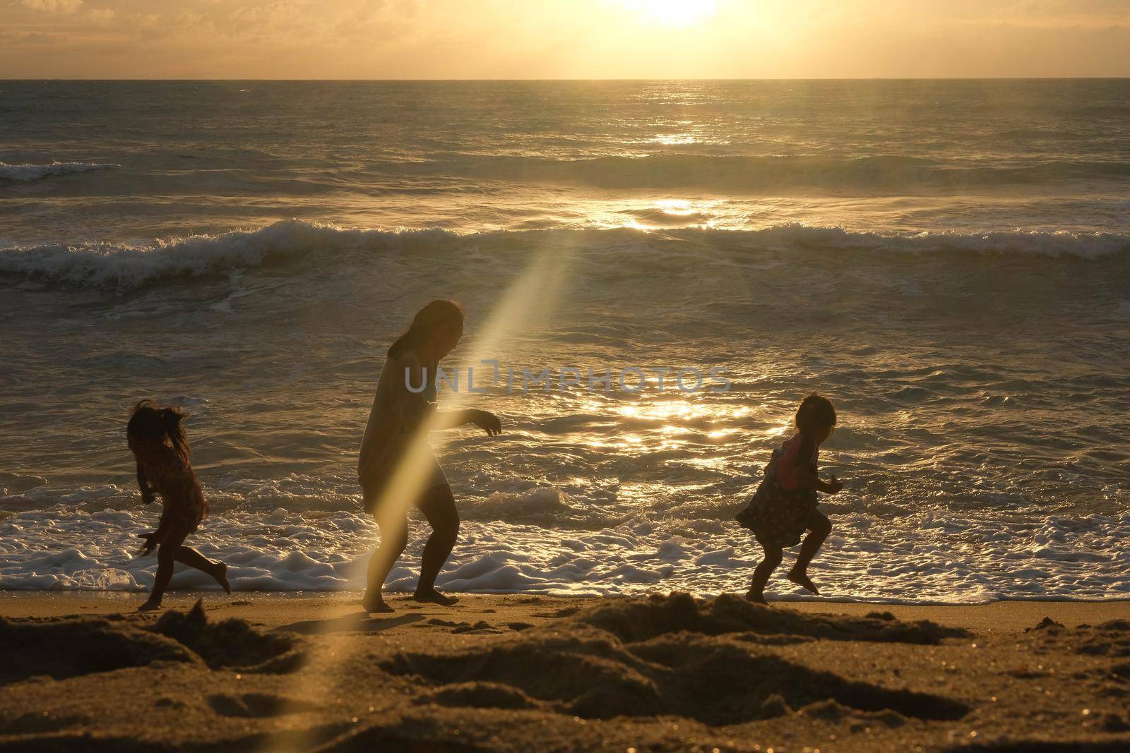 Happy Asian family of mother and daughters having fun playing on the beach during summer vacation at sunset. Summer family trip to the beach. travel and vacation concept.