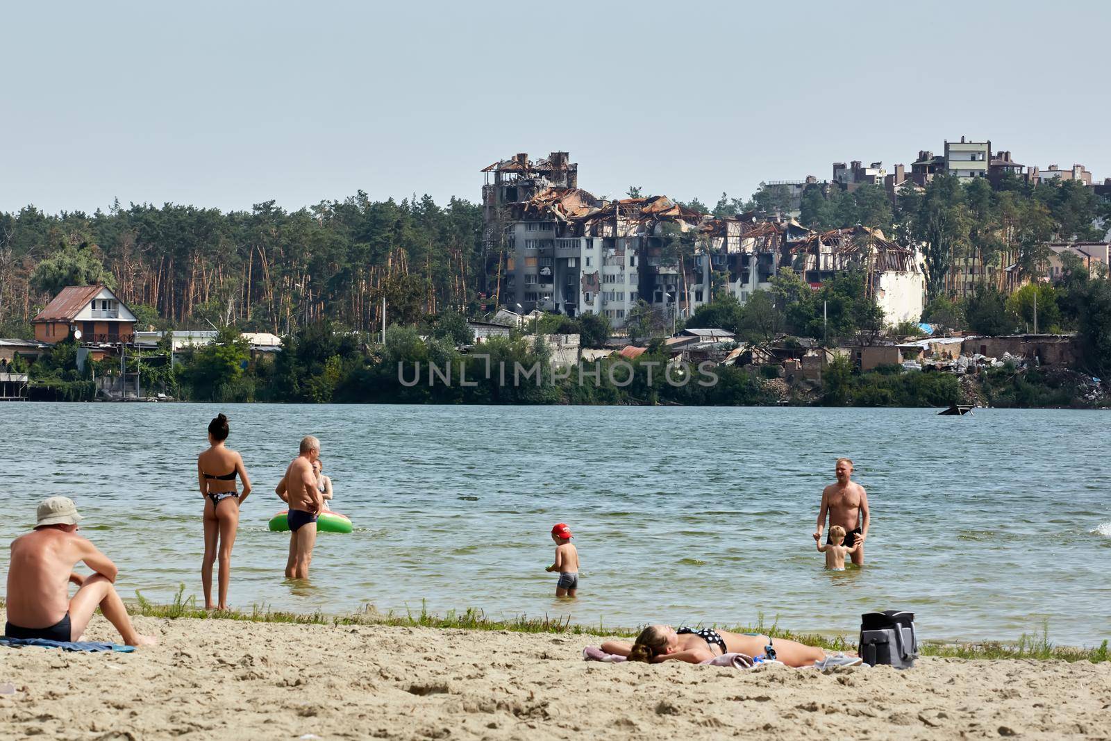 Irpin, Kyiv region, Ukraine - 25 August, 2022: Citi after the Russian occupation. People are having rest near lake opposite destroyed houses