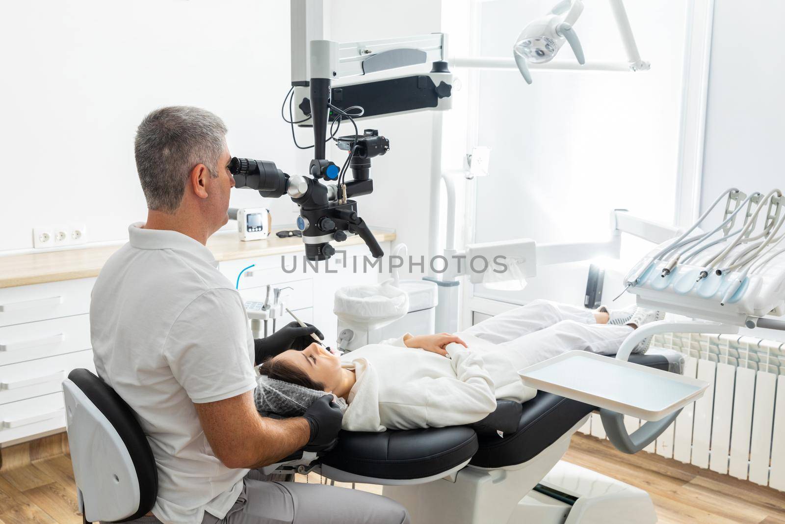 Male dentist using dental microscope treating patient teeth at dental clinic office. Medicine, dentistry and health care concept