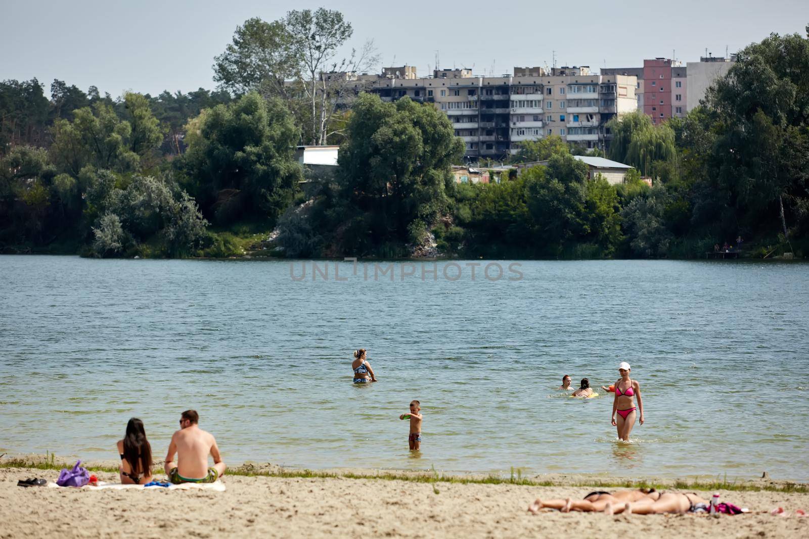 Irpin, Kyiv region, Ukraine - 25 August, 2022: Citi after the Russian occupation. People are having rest near lake opposite destroyed houses. by sarymsakov