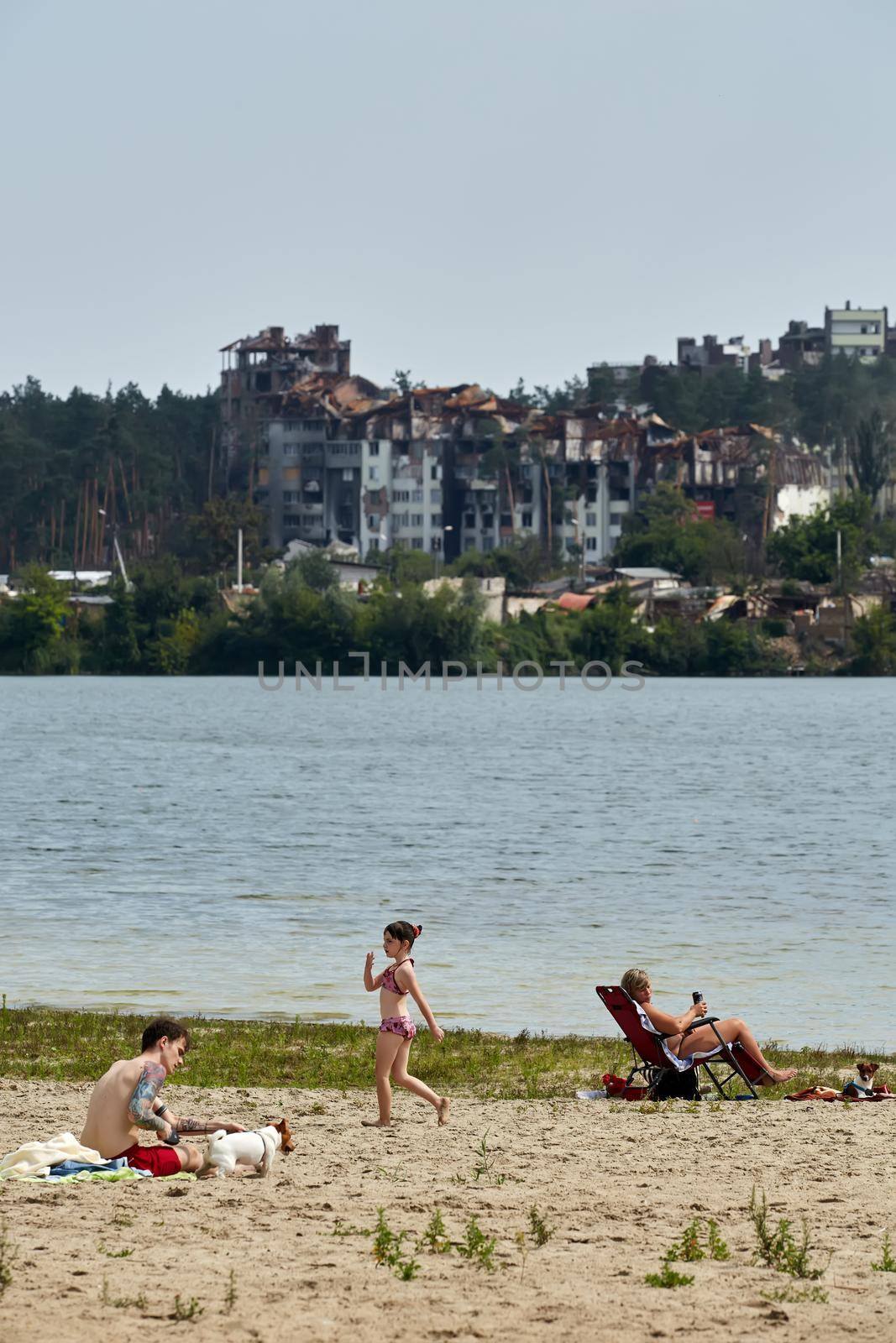 Irpin, Kyiv region, Ukraine - 25 August, 2022: Citi after the Russian occupation. People are having rest near lake opposite destroyed houses