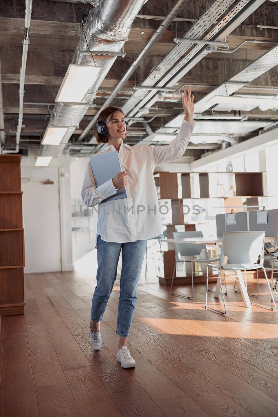 Attractive business woman in headphones with laptop crossing modern office. High quality photo