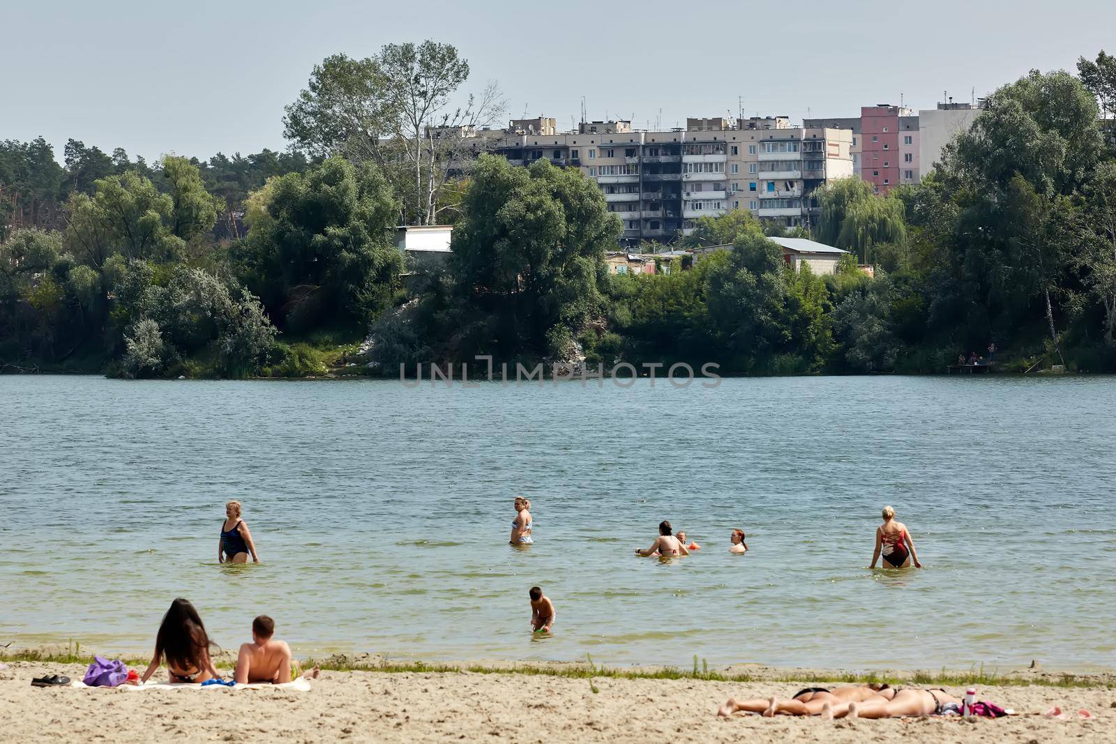 Irpin, Kyiv region, Ukraine - 25 August, 2022: Citi after the Russian occupation. People are having rest near lake opposite destroyed houses. by sarymsakov