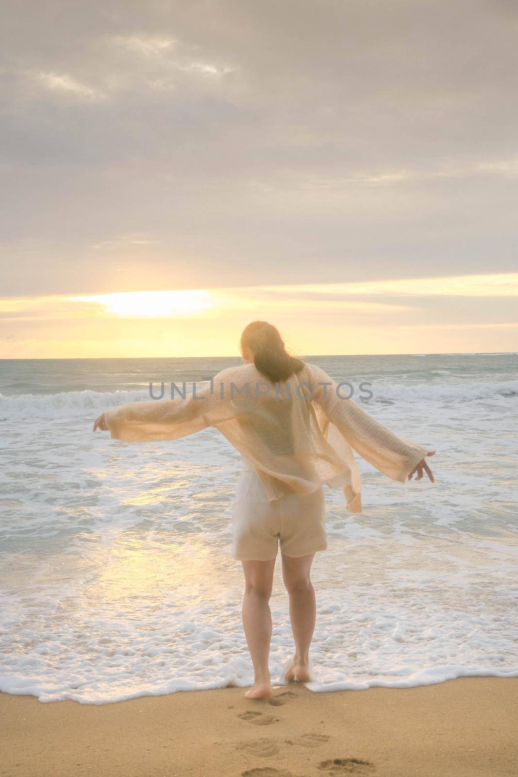 Portrait of a beautiful Asian woman smiling relaxing on the beach. A young woman strolling along the sea looking at the big waves and strong winds. Concept of relaxation and travel on vacation. by TEERASAK