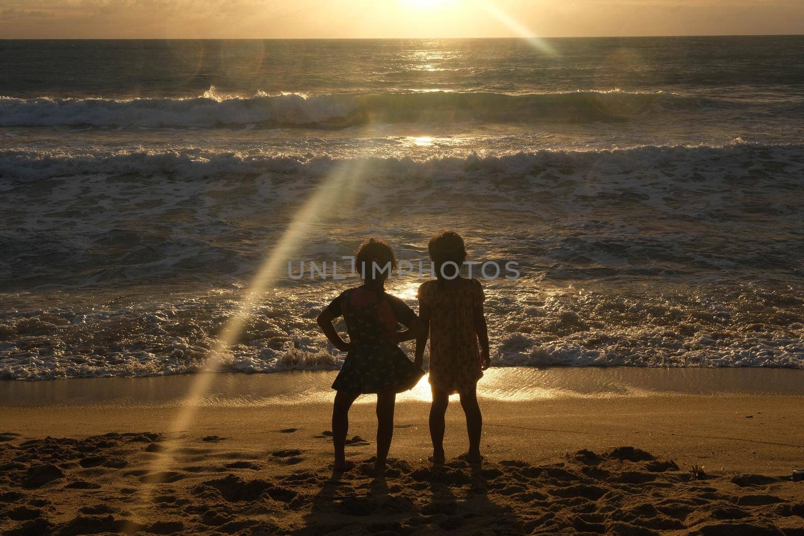 Cute Asian sisters playing on the beach during summer vacation at sunset together. Summer family trip to the beach. travel and vacation concept. by TEERASAK