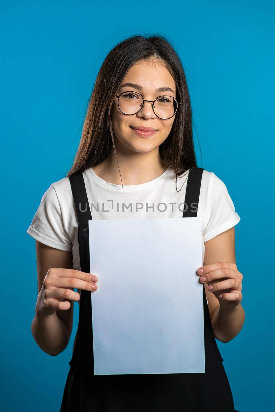 Pretty asian girl holding white a4 paper poster. Copy space. Smiling trendy woman with long hair on studio background