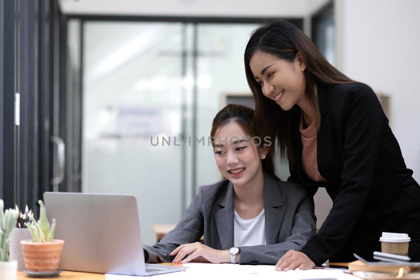 Two young Asian businesswoman discuss investment project working and planning strategy. Business people talking together with laptop computer at office..