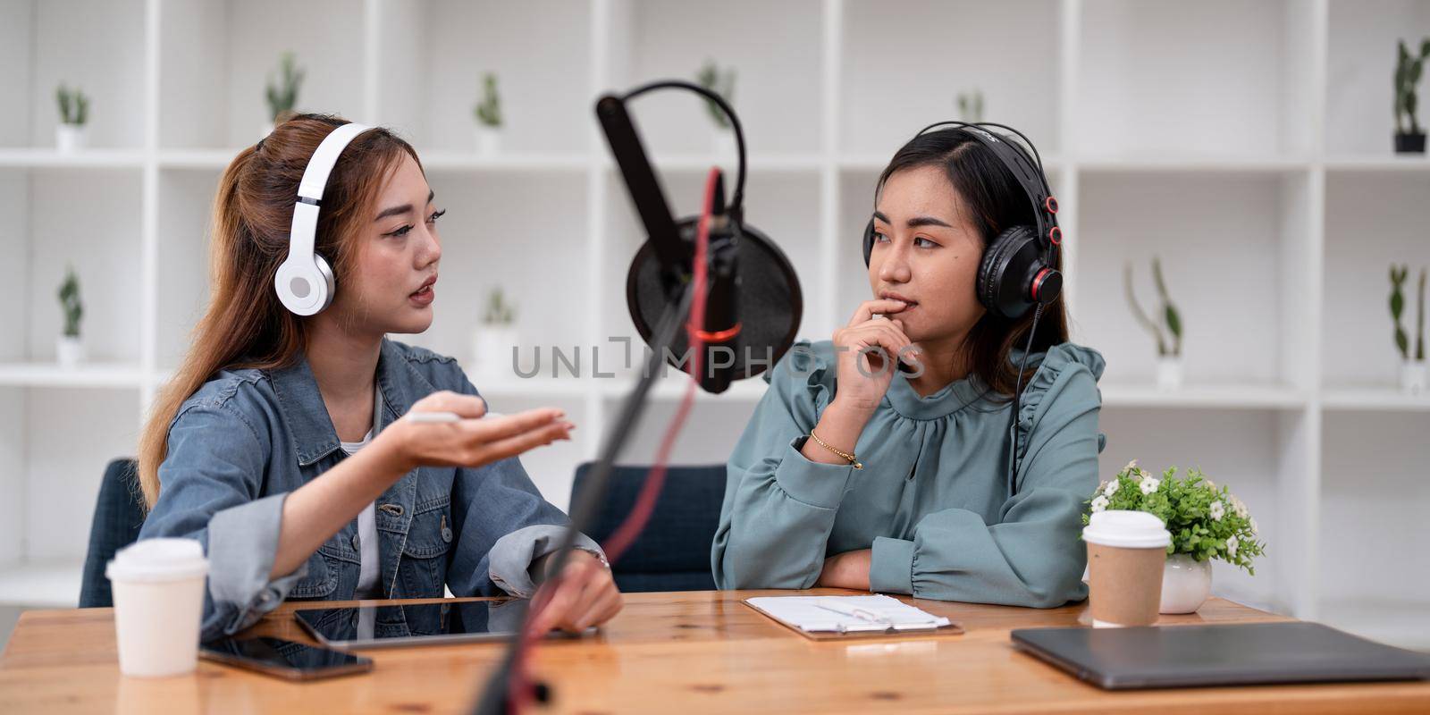 Asian female host recording radio podcast interview with guest at home office.