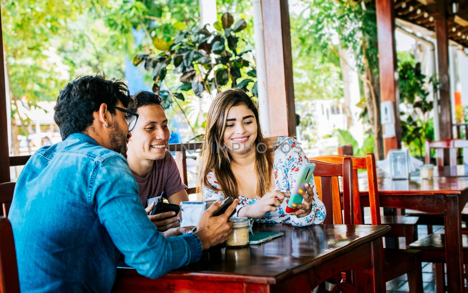 Young friends in a coffee shop with their cell phones having a good time. Three people in a coffee shop with phones having a good time. Three teenage friends on their cell phones in a coffee shop by isaiphoto