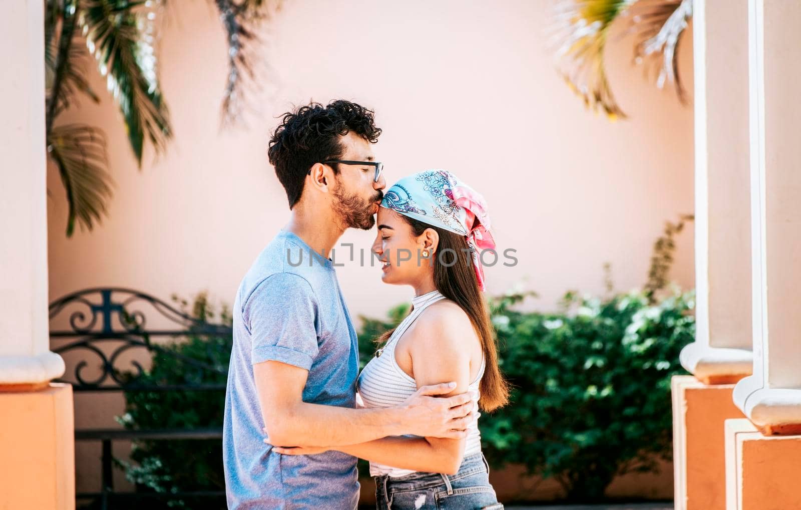 Man kissing his girlfriend forehead outside. Cute couple embracing the boyfriend kisses the girl forehead. Portrait of beautiful couple in love. Boyfriend tenderly kissing his girlfriend forehead by isaiphoto