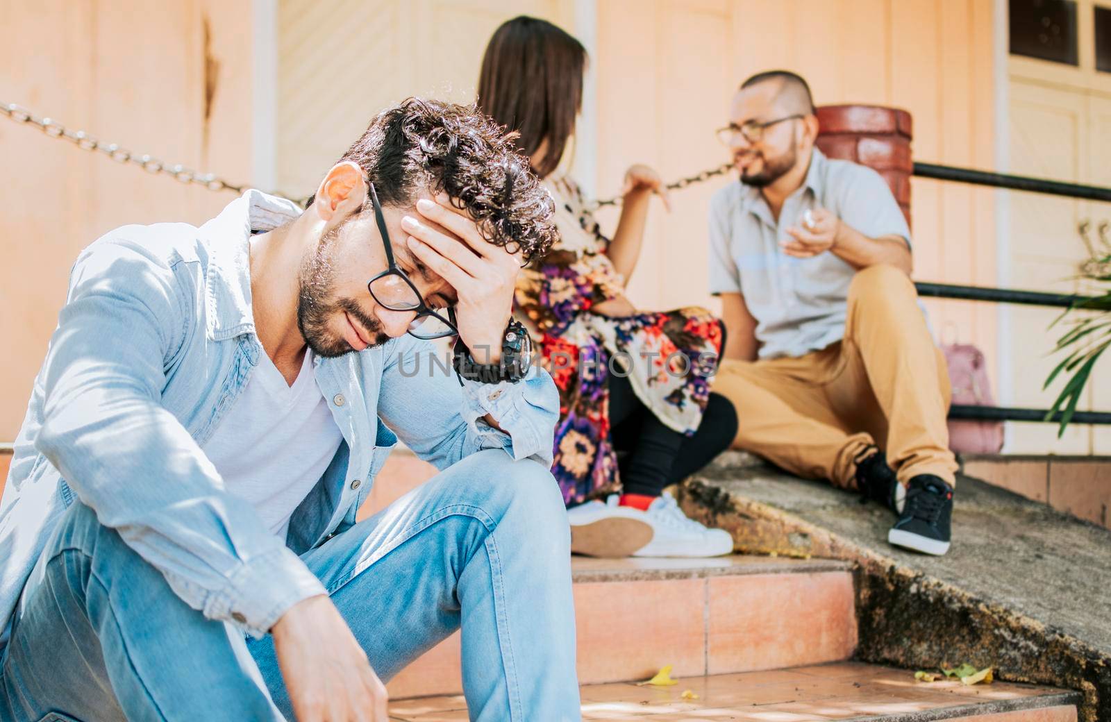 Sad man seeing his girlfriend cheating with his friend. Sad boyfriend sitting on some stairs while his girlfriend talking to another man. Girl talking to another man and her boyfriend is offended