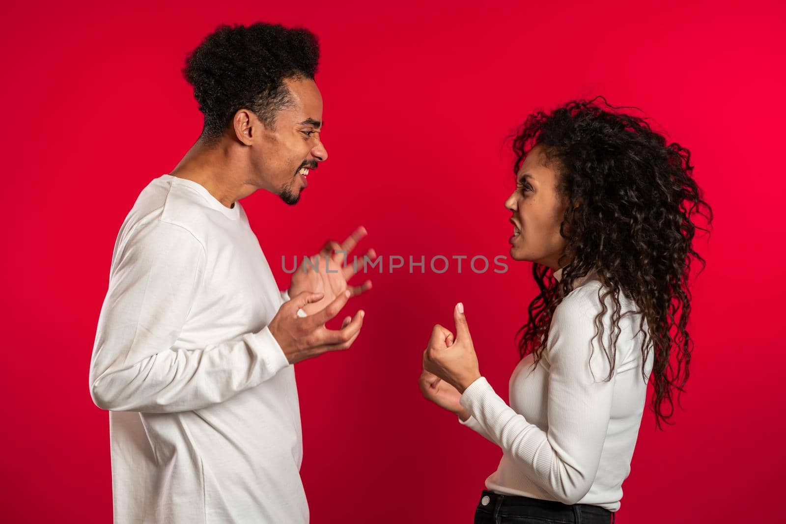 Young african american match emotionally quarreling on red background in studio. Concept of conflict, problems in relationships.