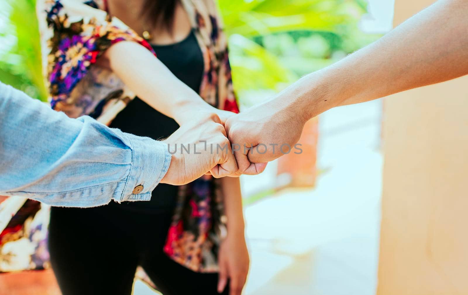 Close up of three friends bumping fists, Concept of friends fist bumping outdoors. Front view of three friends bumping fists in the street. Concept of union and commitment of friends.