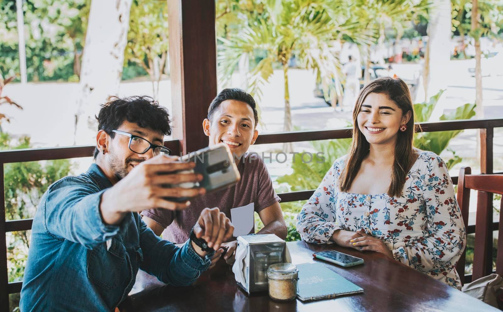 Young friends taking a selfie in a coffee shop. Three happy people in a coffee shop taking a selfie. Front view of teenage friends taking selfie and having fun in a cafe restaurant by isaiphoto