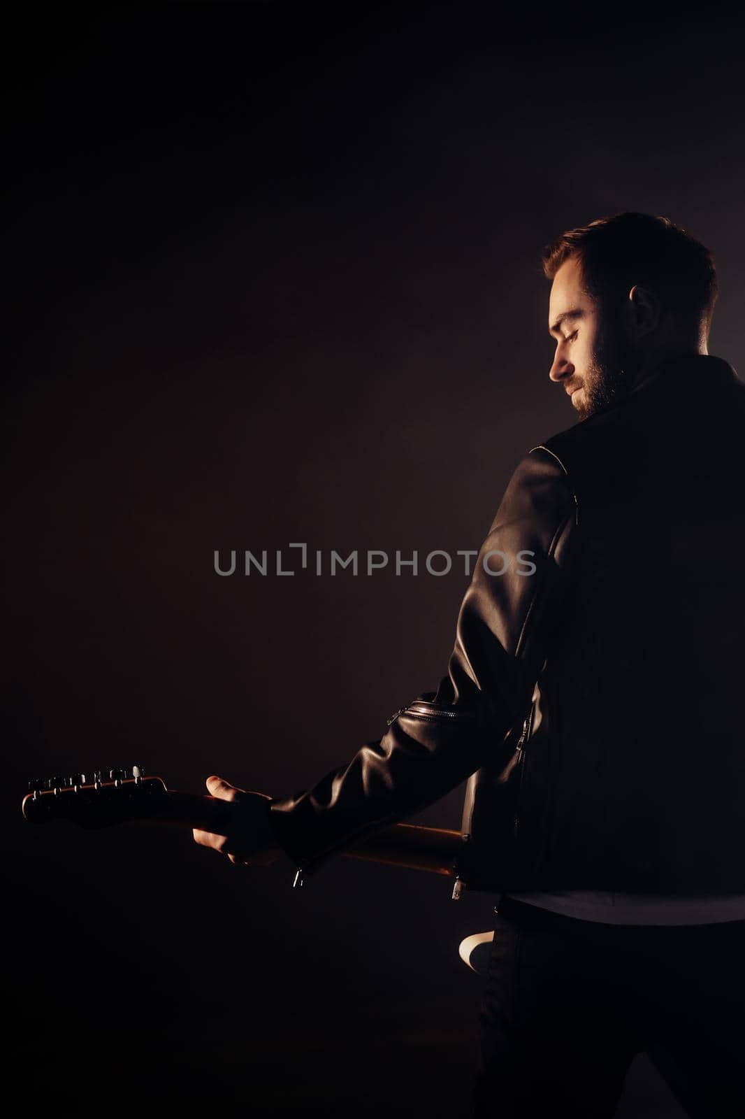 Rock guitarist man in leather jacket in smoky studio or stage masterfully playing electric guitar. View of musician in the spotlight