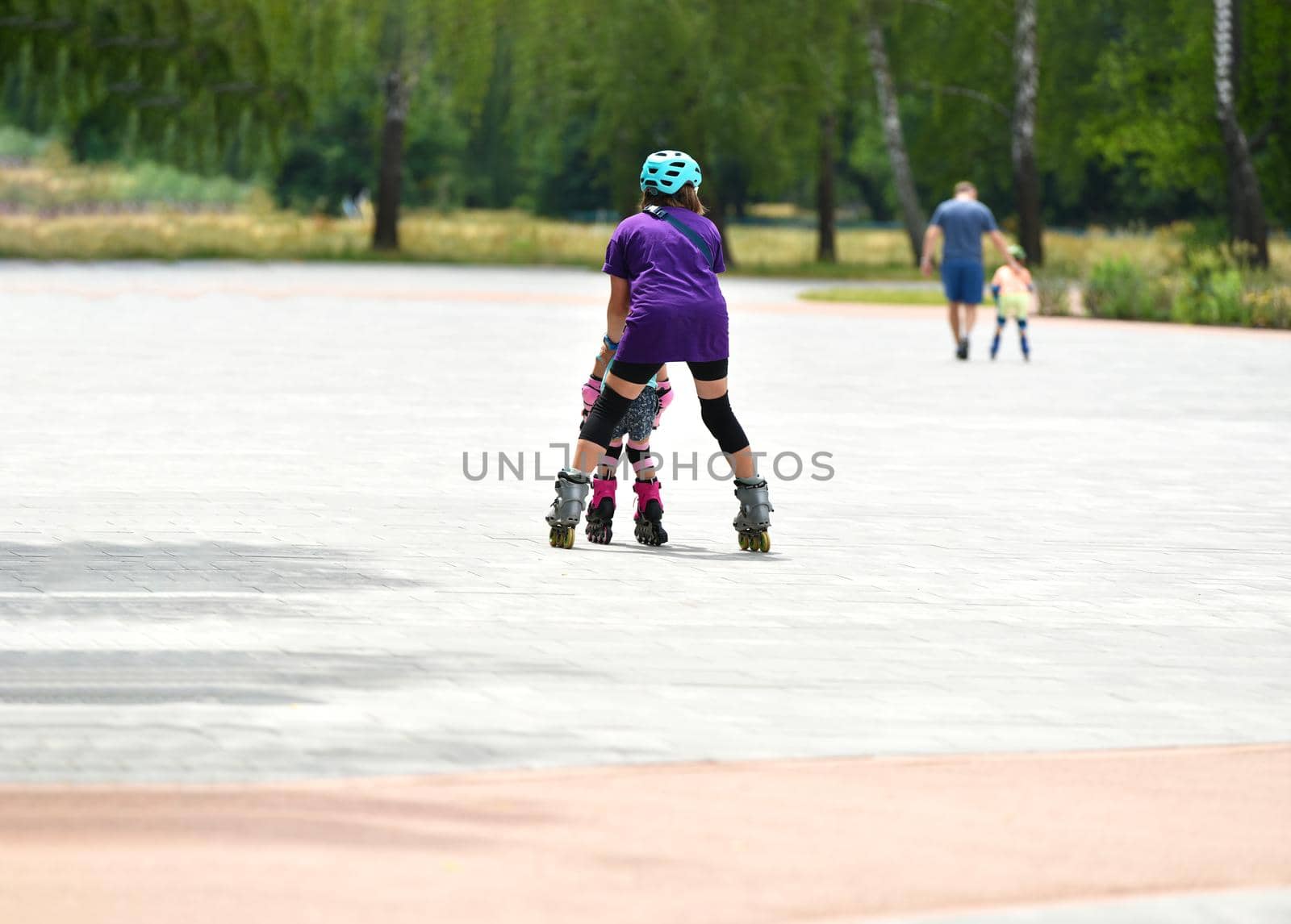 Young mother and her little daughter rollerskating in summer park. by Suietska