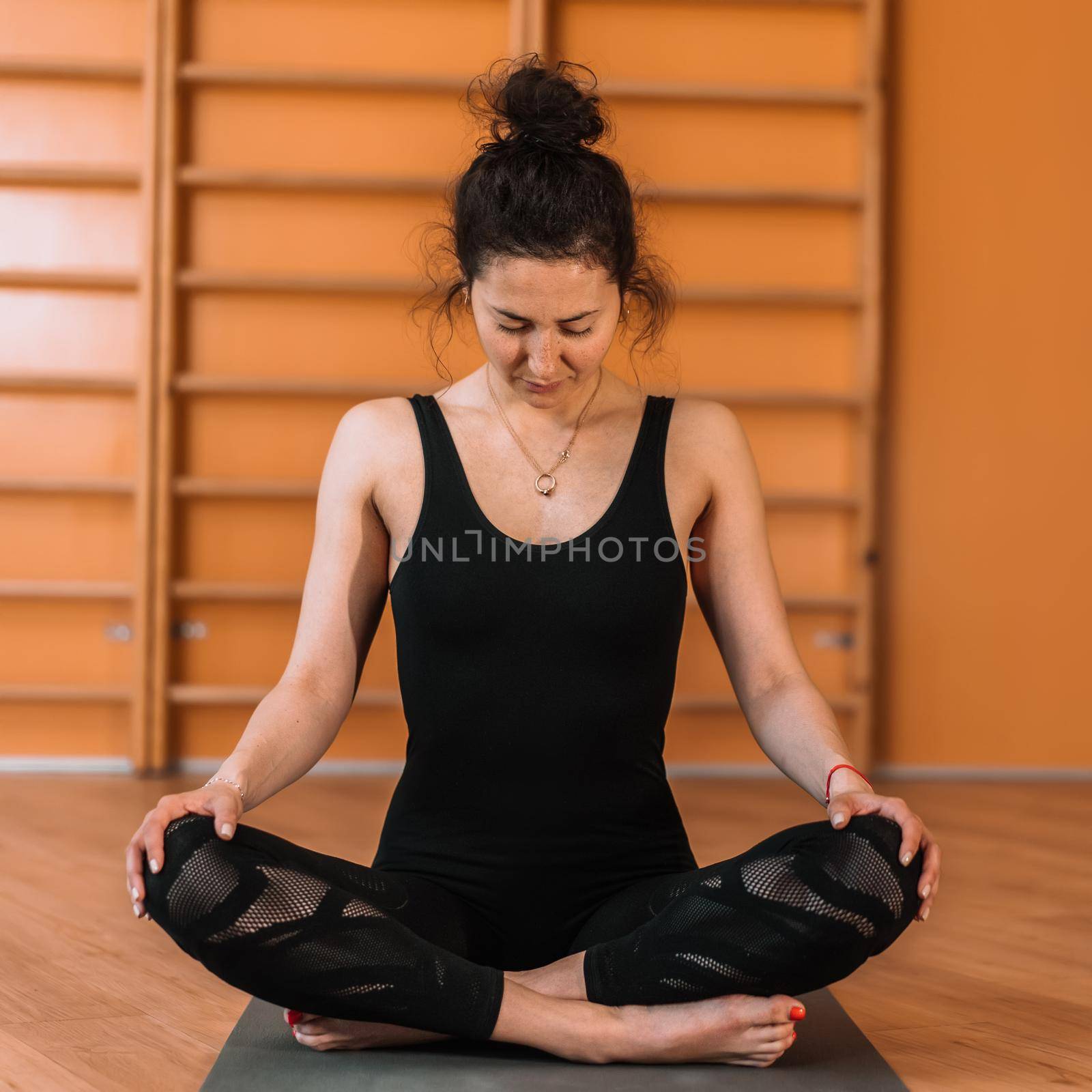 Woman in black practicing yoga at light minimalist studio class room. Lady sitting in lotus pose. Health lifestyle concept by kristina_kokhanova
