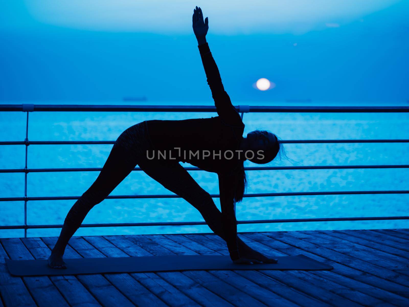 Yoga under full moon over night ocean or sea beach. Young woman's meditation during practice