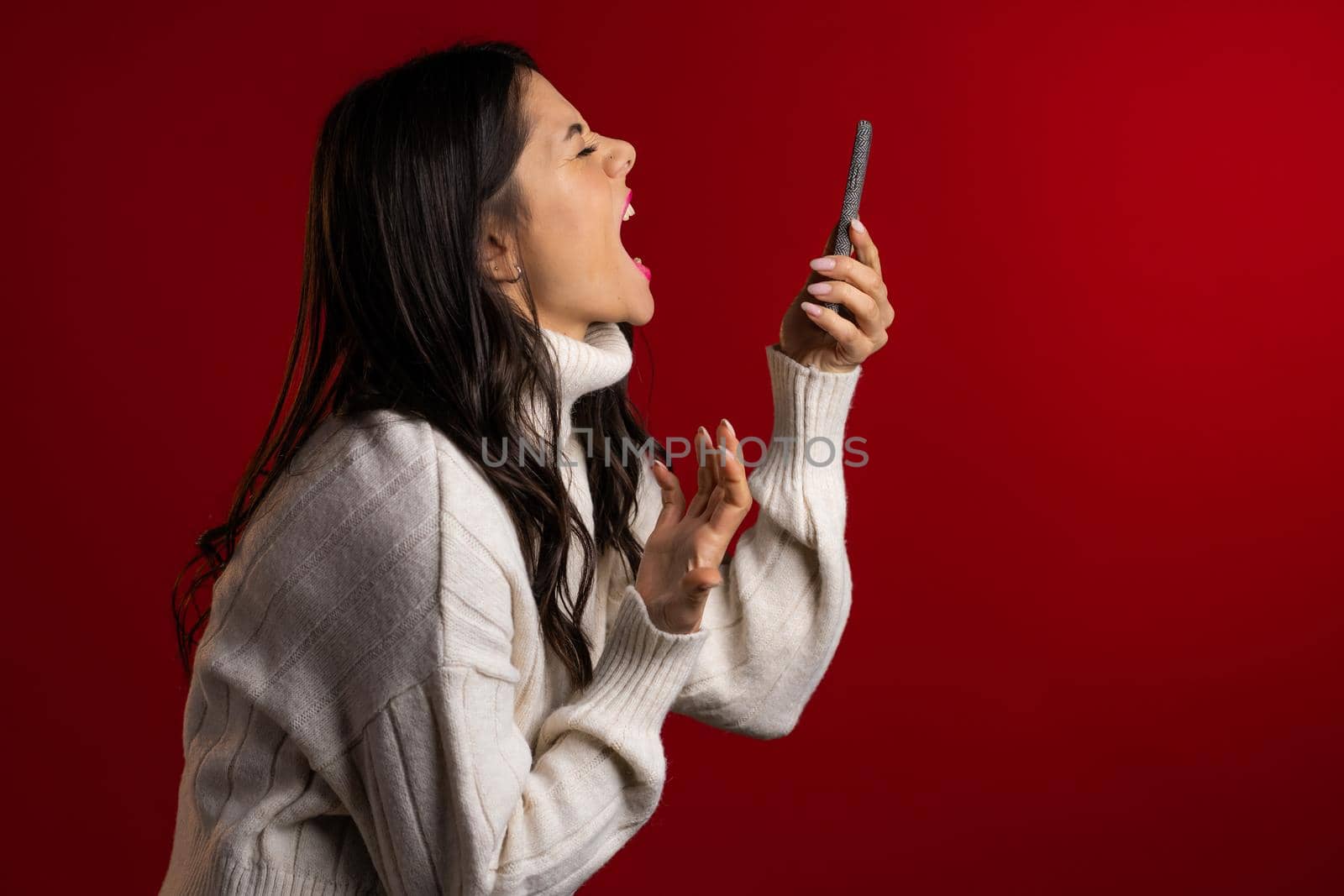 Angry woman screaming down, swears with somebody. Using mobile phone. Stressed and depressed girl on red background.
