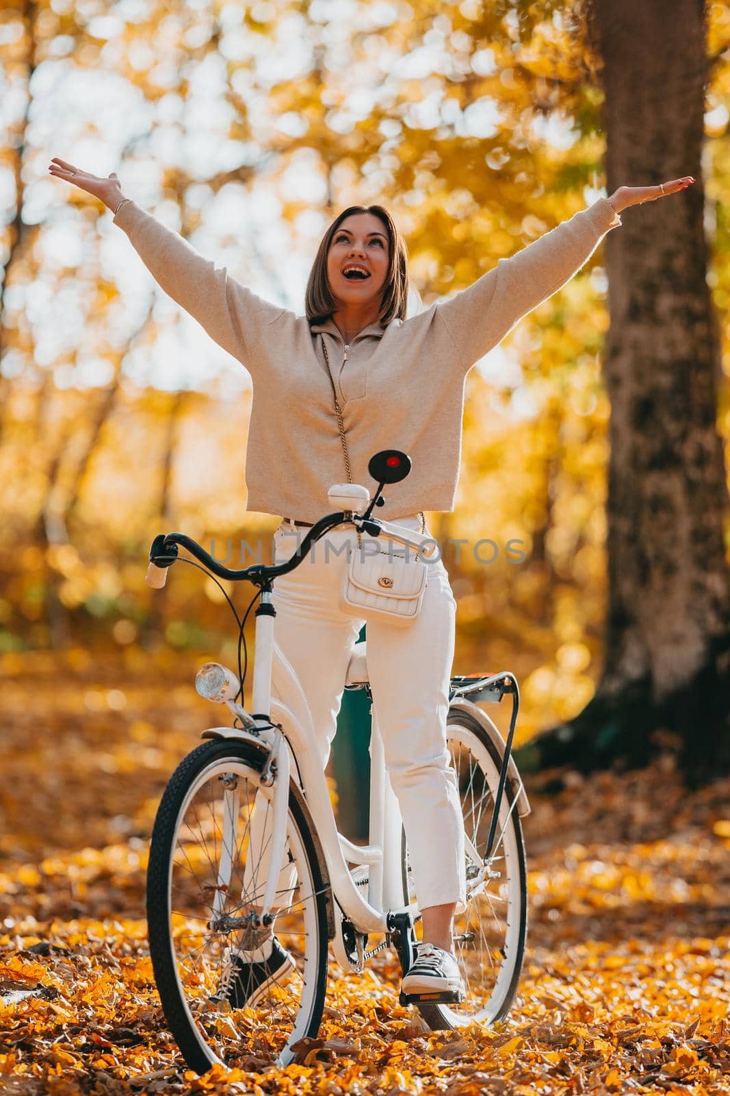 Young woman in cozy outfit rejoices autumn, freedom and beautiful nature. Girl with open hands. Love, gratitude concept. Amazing scene of trendy girl with bicycle. by kristina_kokhanova
