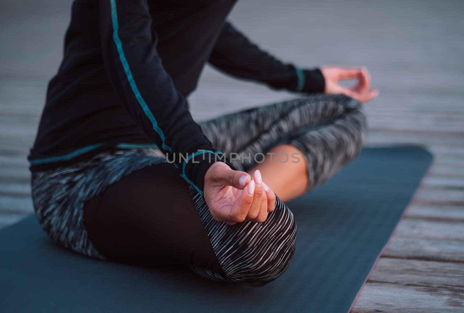 Unrecognizable concentrated woman in black practicing in yoga meditation on wooden seafront. Woman in lotus pose. Stretching, practice, healthy lifestyle concept. by kristina_kokhanova