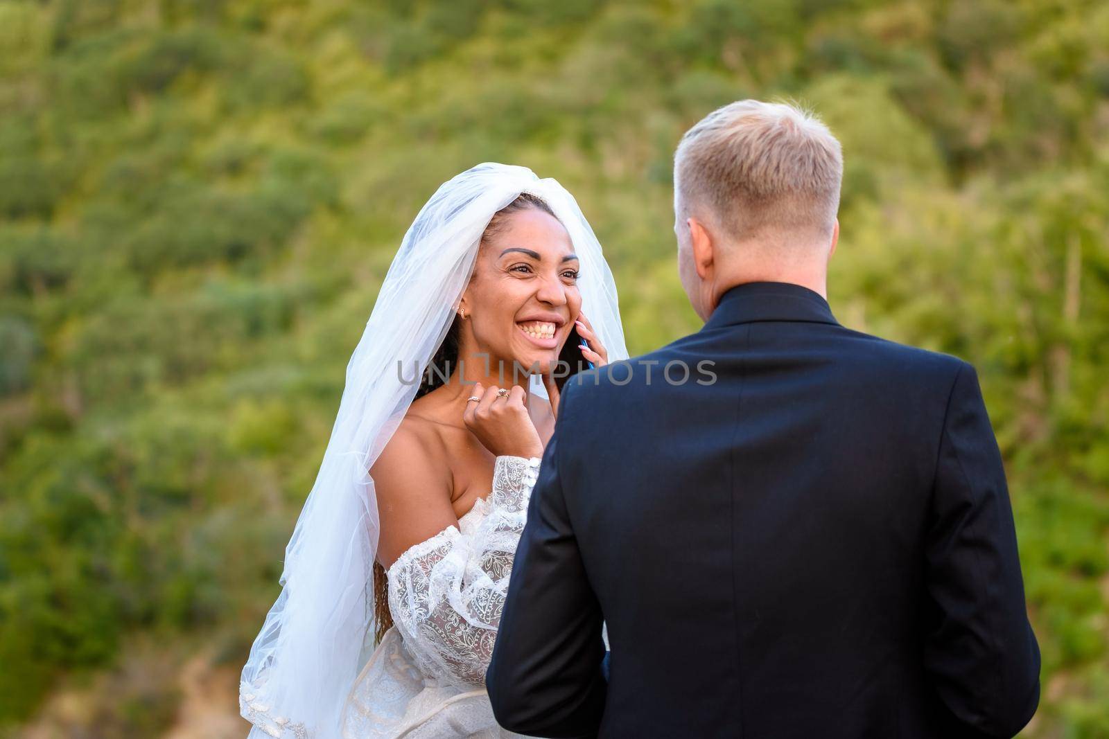 Black bride talking on the phone and looking happily at her white husband