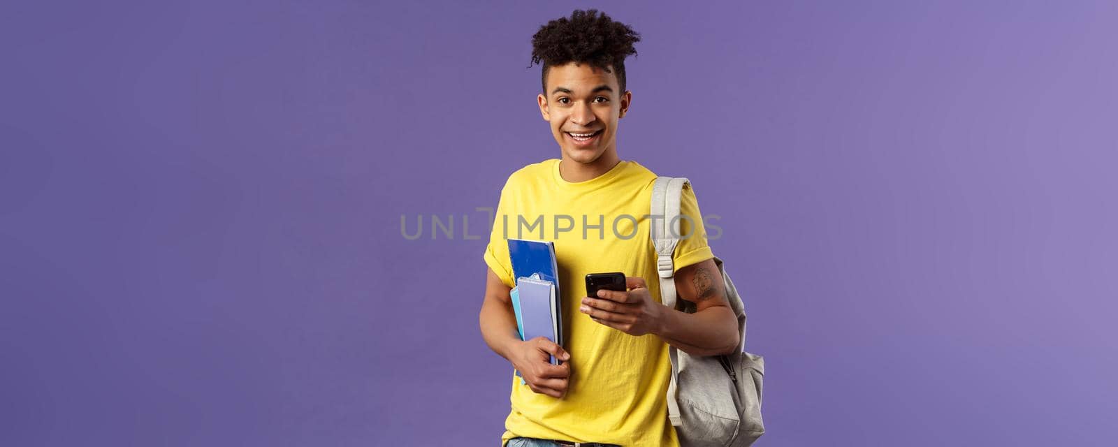 Back to school, university concept. Portrait of young handsome smiling man, student asking for classmate phone number, making note in mobile phone, wear backpack, hold notebooks and study material by Benzoix