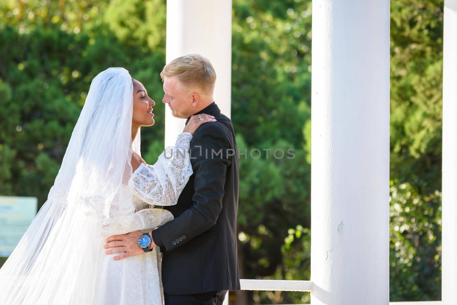 Mixed-racial newlyweds on a walk hugging and lovingly look at each other