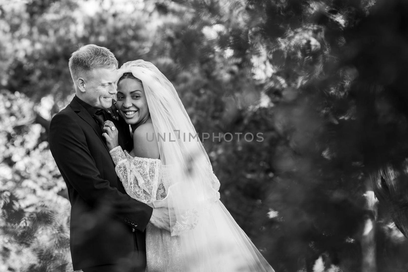 Portrait of interracial newlyweds hugging against the backdrop of a beautiful forest landscape, black and white photography