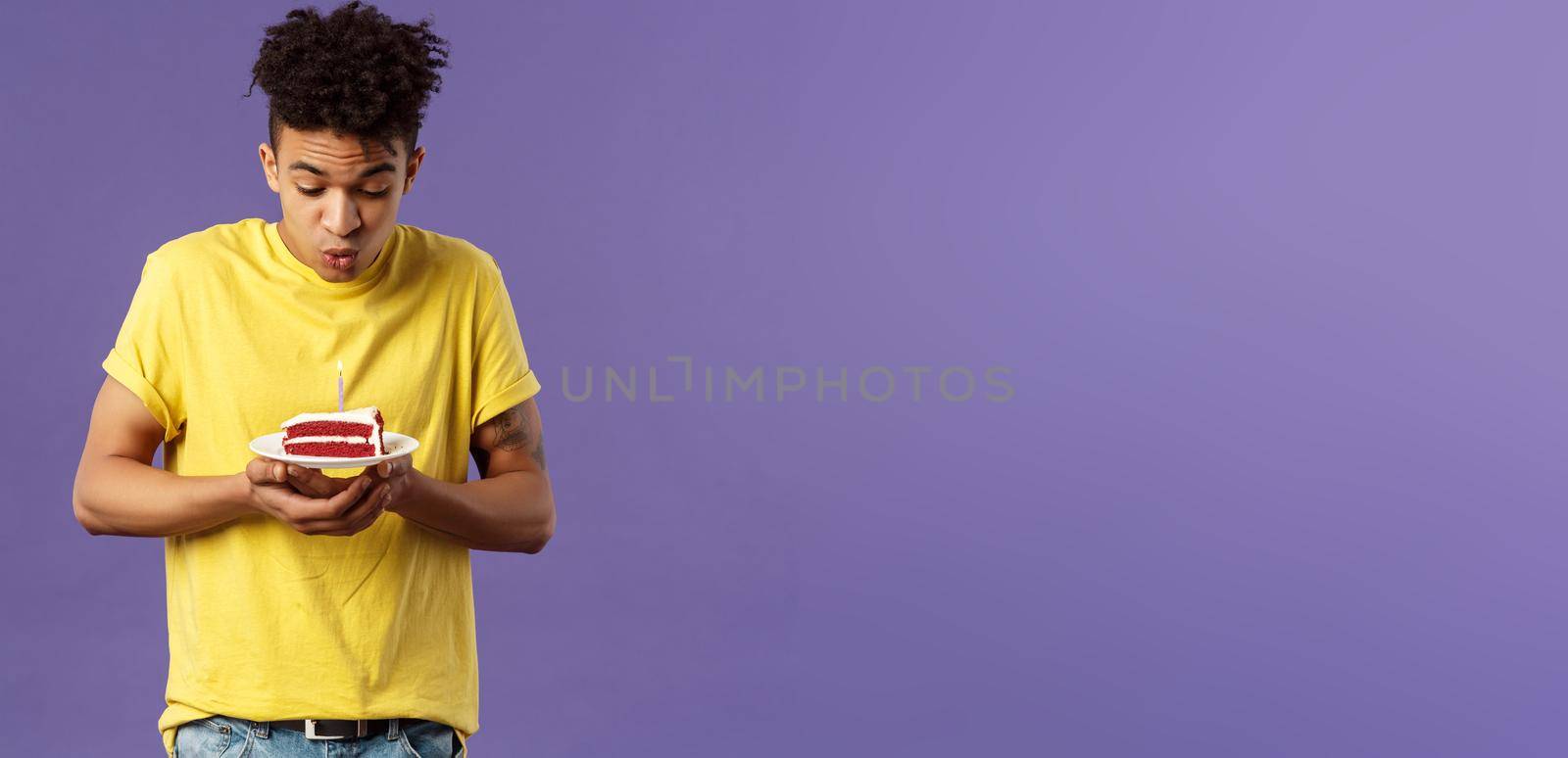 Portrait of cute excited young guy with dreads and tattoos, making wish on birthday, celebrating party, blowing candle on b-day cake, standing purple background dreaming by Benzoix