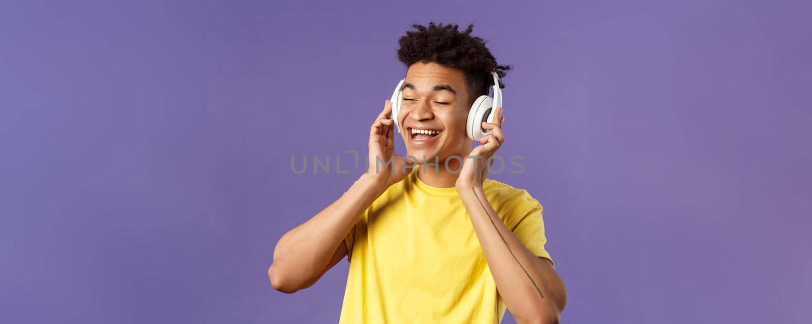 Close-up portrait of carefree, young upbeat man with dreads, close eyes and smiling pleased as listening to awesome new song favorite artist uploaded music platform, wear headphones by Benzoix