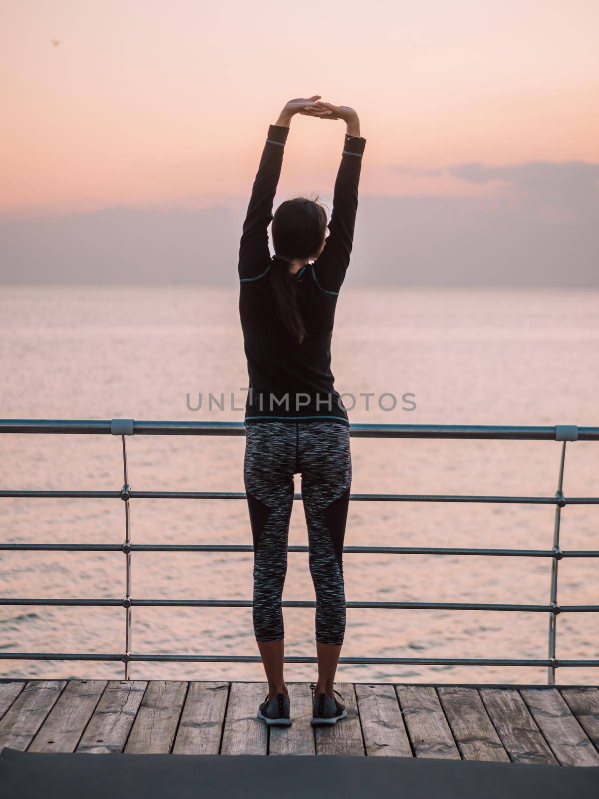 Young sexy sports woman stretches. Girl standing on yoga mat. Sea or ocean background. Summer days