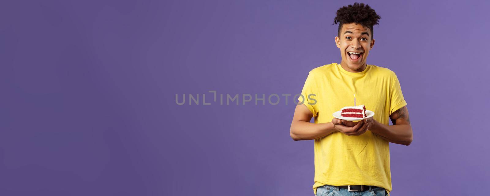 Happy birthday to me. Portrait of upbeat, excited hispanic man with dreads celebrating b-day, holding plate cake with lit candle, smiling amused, making wish, purple background.