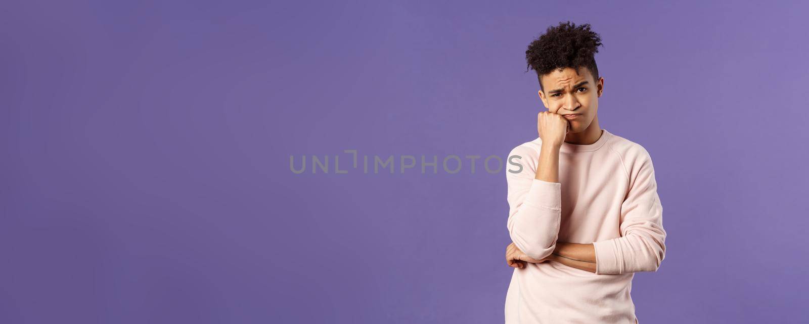 Portrait of complicated, troubled young hispanic man facing tough problem, lean on fist grimacing and pouting, solving troublesome situation, thinking, feeling uneasy, purple background.