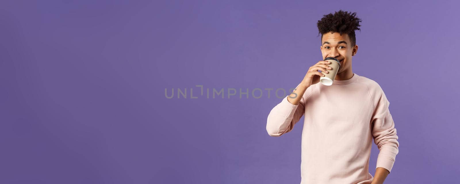 Leisure, lifestyle and people concept. Portrait of young cheerful guy drinking coffee take-away from favorite cafe, smiling enjoying nice spring day, standing purple background.