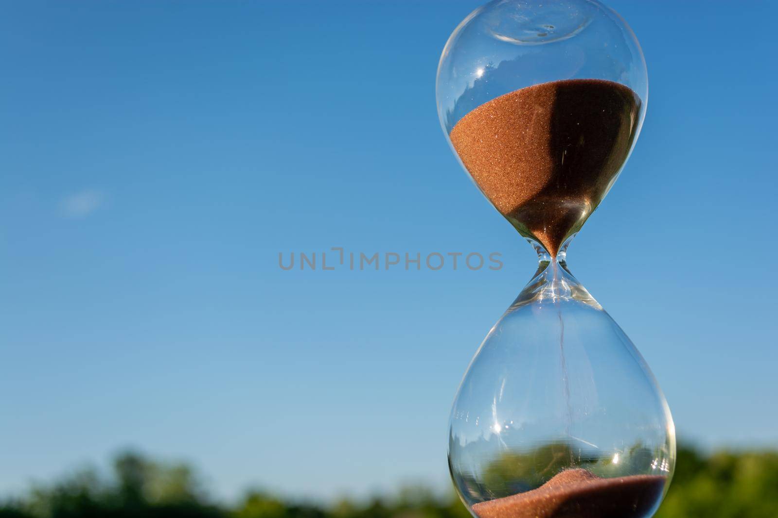 Hourglass against the blue sky on a sunny day. Changeable weather symbol.