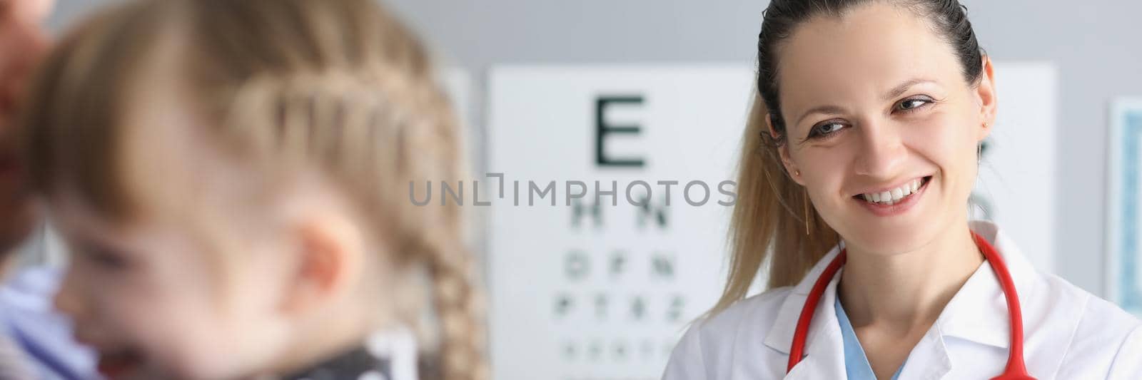 Smiling female doctor standing near little girl in clinic by kuprevich