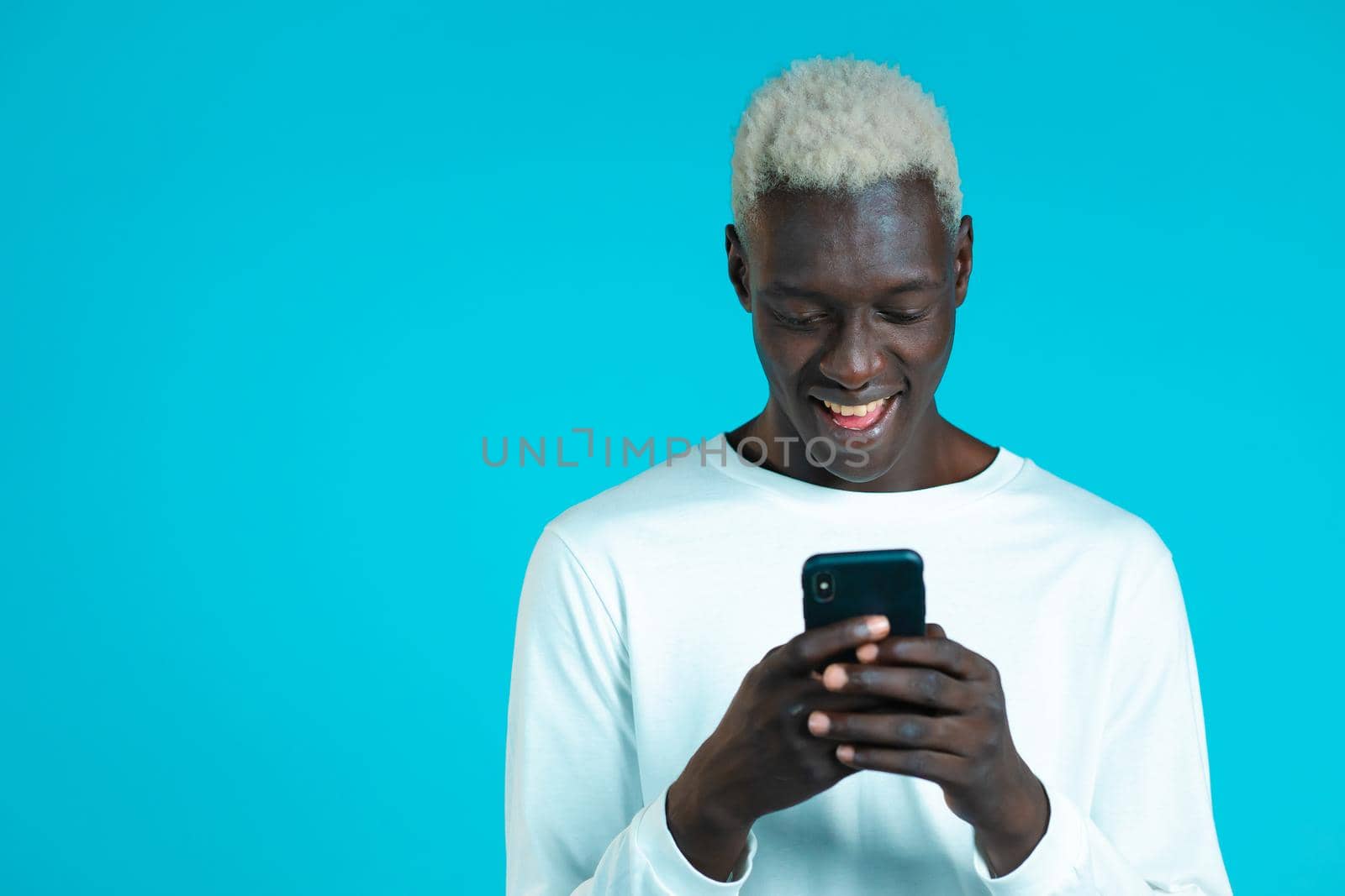 Handsome african man playing game on smartphone on blue studio wall. Using modern technology - apps, social networks