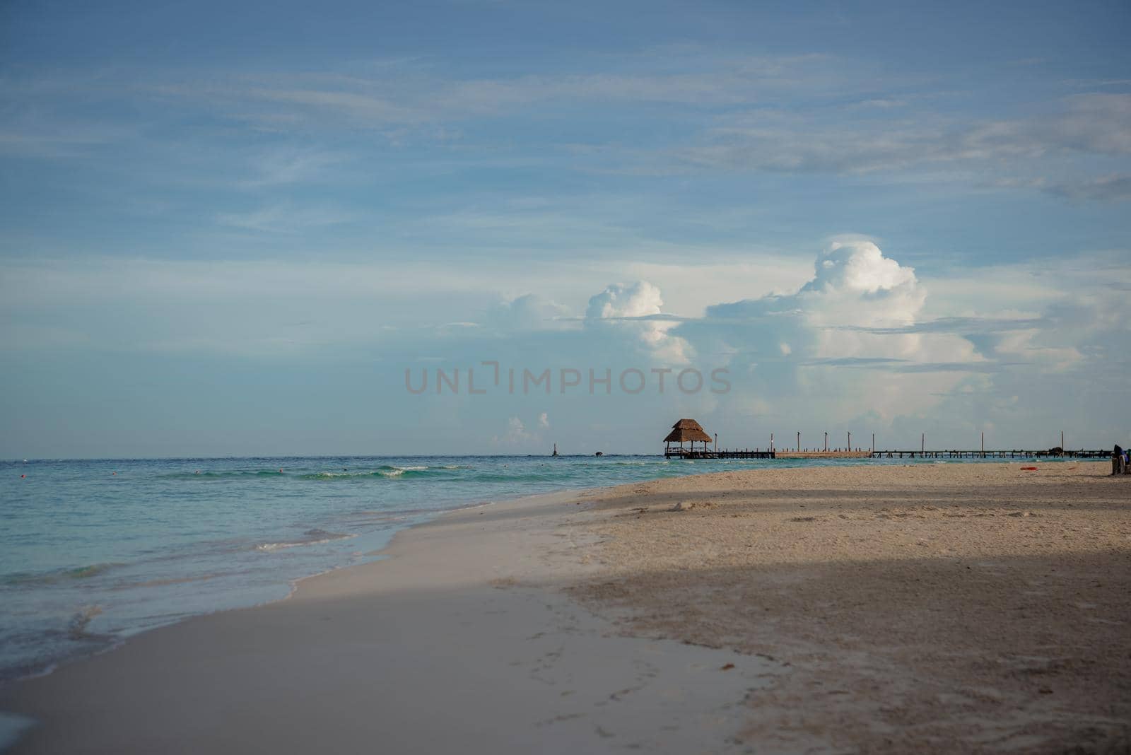 Sandy Caribbean Sea beach with azure water and thatched hut on the horizon.