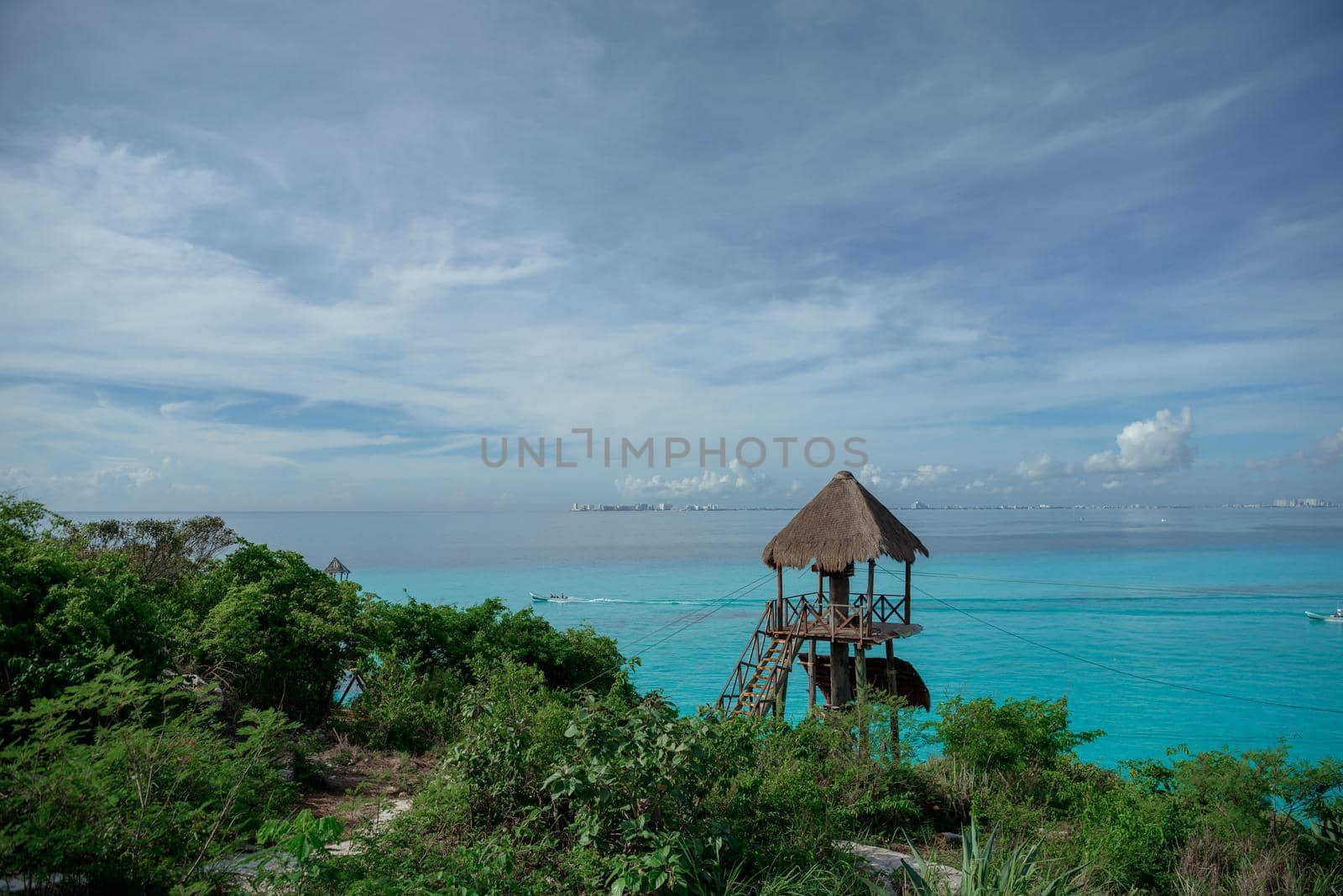 Sandy Caribbean Sea beach with azure water and thatched hut on the horizon.