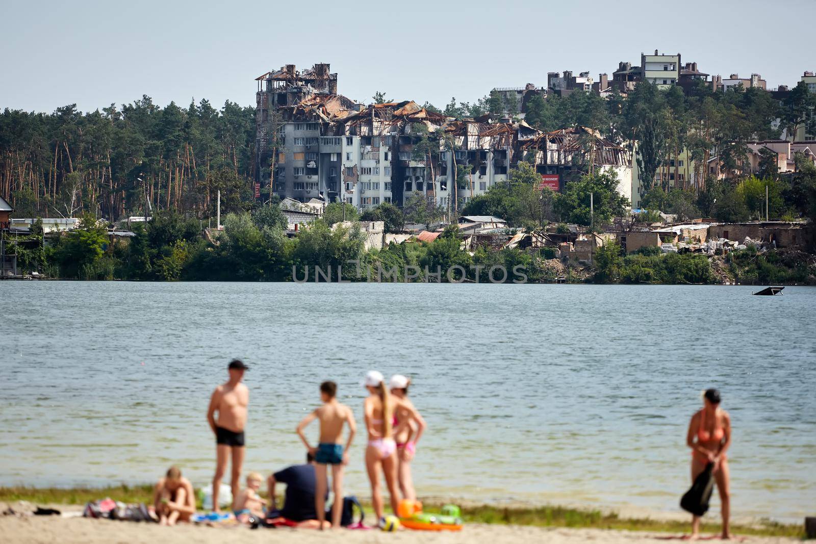 Irpin, Kyiv region, Ukraine - 25 August, 2022: Citi after the Russian occupation. People are having rest near lake opposite destroyed houses